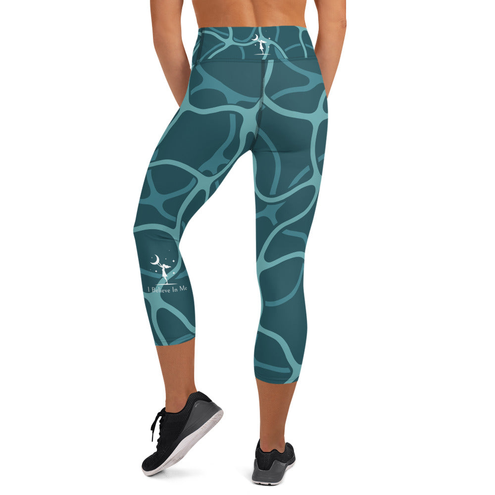 rear view of a barefoot woman wearing aqua colored capri length yoga pant with a teal design