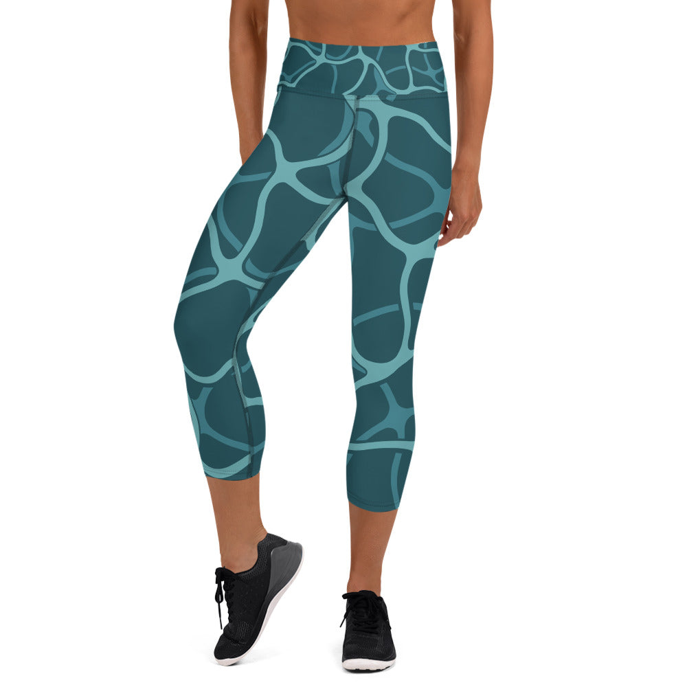 front view of a barefoot woman wearing aqua colored capri length yoga pant with a teal design