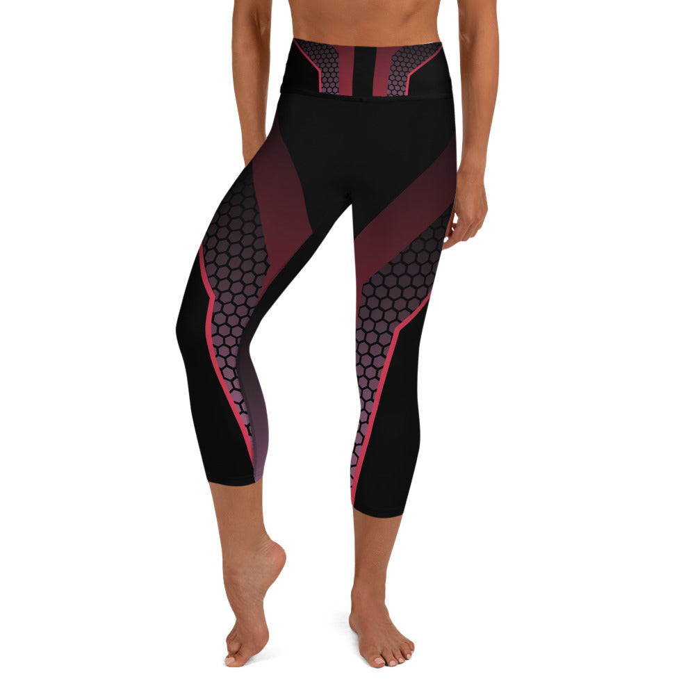 front view of a barefoot woman wearing black capri length yoga pants. The pants feature a exciting geometric pattern of different shades of pink